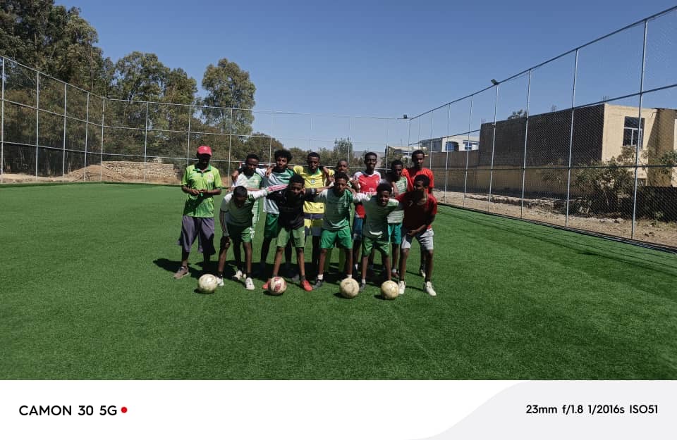 Players pose together on a green football pitch with balls
