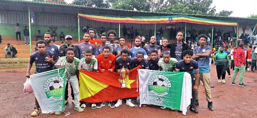 Group of Green Star players gathered with a trophy and club banners at a football ground